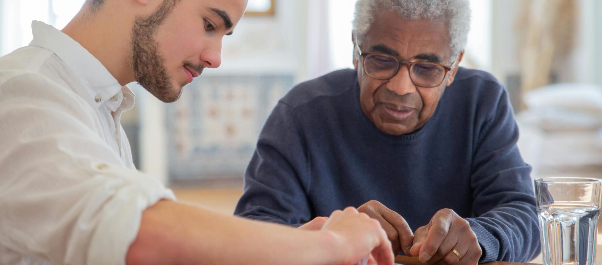 A young volunteer helps an elderly man manage his medication at a nursing home.