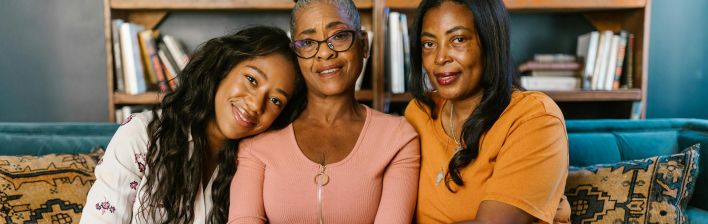Three beautiful black women sitting together on a couch, smiling indoors.