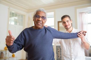 Elderly man smiling with caregiver in a supportive home environment, promoting health and happiness.